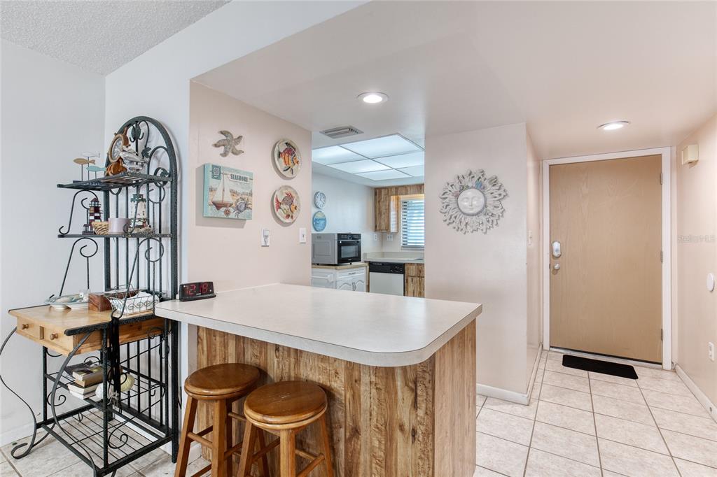 A kitchen features a breakfast bar with wooden paneling, two stools, and tile flooring — 1275 OCEAN SHORE BOULEVARD UNIT 2030, ORMOND BEACH, FL
