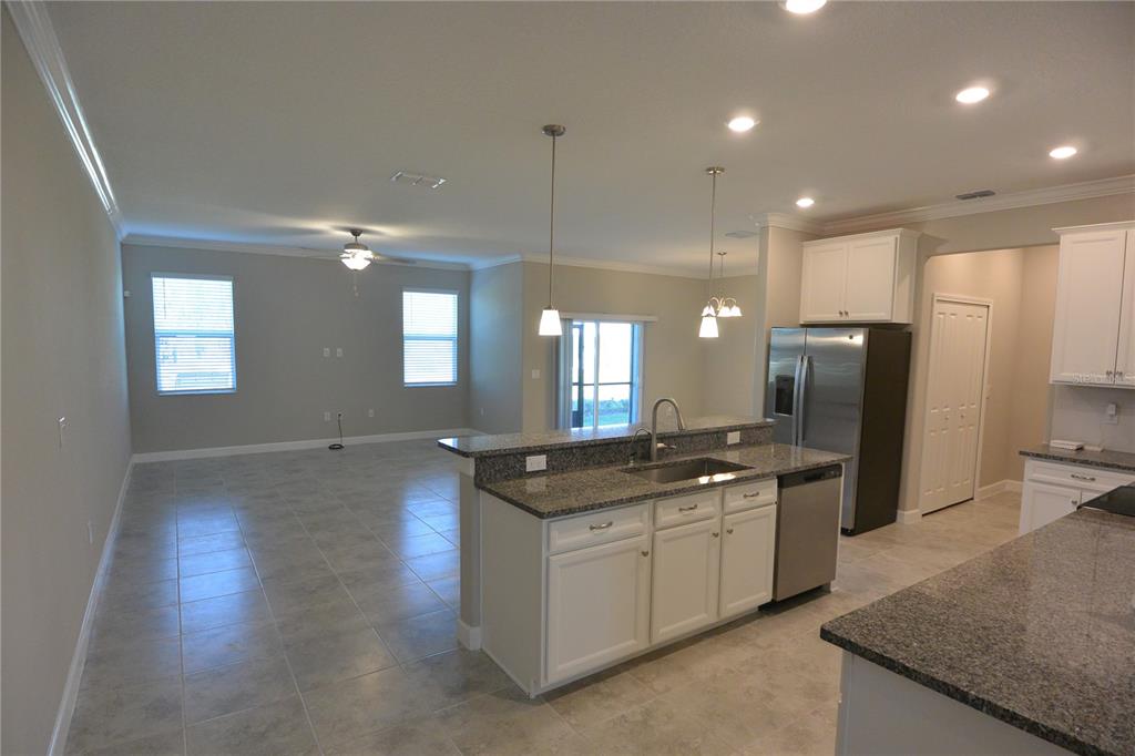 A kitchen with granite countertops and white cabinets overlooks an open-concept living area with tile — 2277 CERULEAN SKY DRIVE, LUTZ, FL