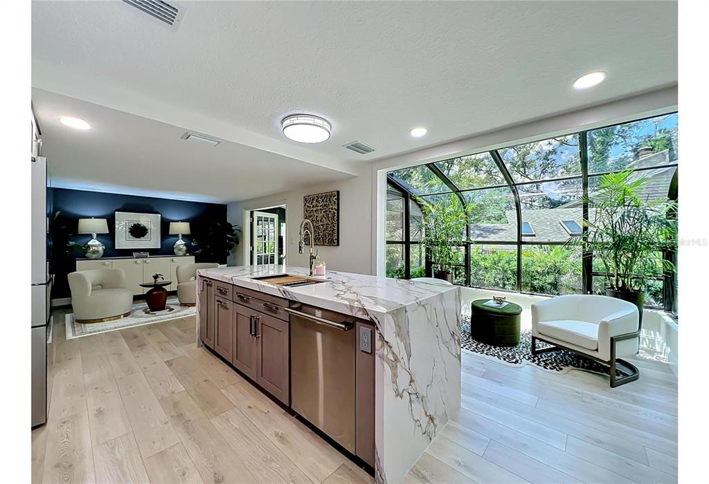 A modern kitchen with a marble island opens to a sunroom through glass doors — 128 WOODMILL ROAD, LONGWOOD, FL