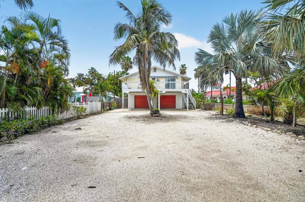 A two-story house with two red garage doors stands behind a large gravel driveway — 524 SPRING AVENUE, ANNA MARIA, FL