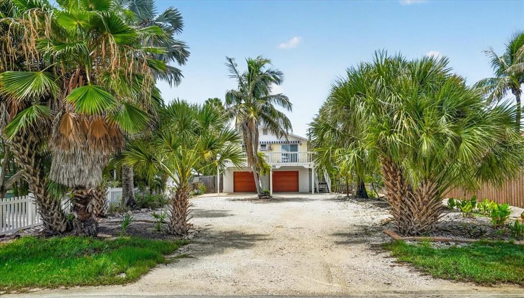 A two-story house with two orange garage doors sits behind a gravel driveway and palm trees — 524 SPRING AVENUE, ANNA MARIA, FL