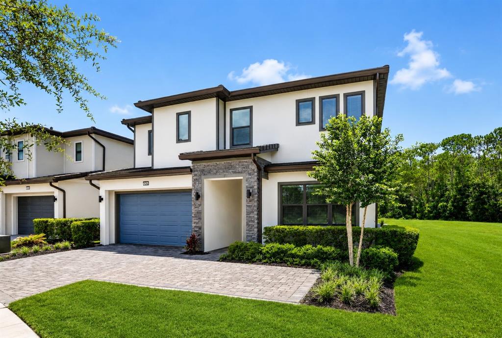 A two-story house with a blue garage door, stone accents, and a paved driveway — 1242 BUTTERFLY ORCHID ROAD, DAVENPORT, FL
