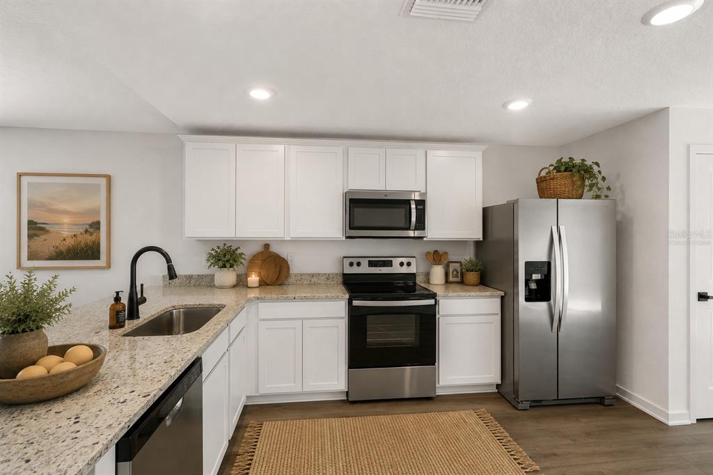 A kitchen features white cabinets, granite countertops, stainless steel appliances, and a woven area rug — 7172 CANOPY LANE, LAKELAND, FL