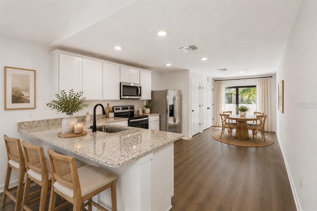 A kitchen with white cabinets, granite countertops, and a dining area with a round table — 7172 CANOPY LANE, LAKELAND, FL
