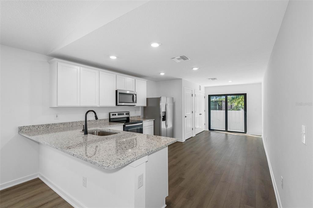 A kitchen with white cabinets, granite countertops, and stainless steel appliances opens to a living area — 7172 CANOPY LANE, LAKELAND, FL