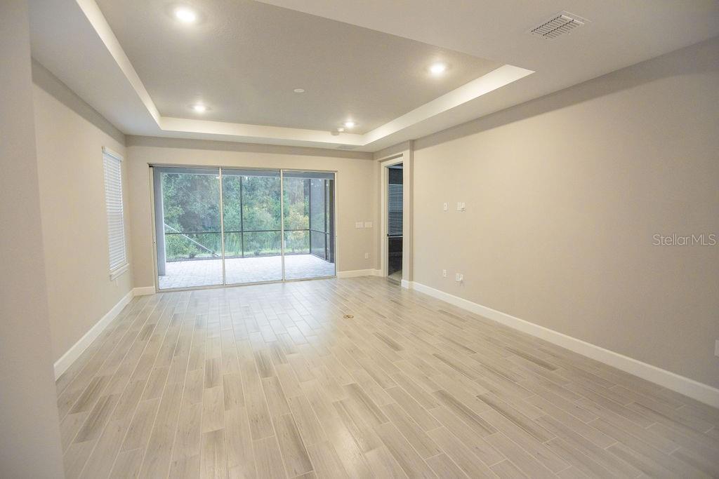 A living room with light tile flooring, a tray ceiling, and sliding glass doors — 4605 ROSATTI ROAD, WESLEY CHAPEL, FL