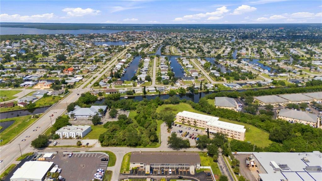 An aerial view shows a suburban neighborhood with canals, residential buildings, and commercial properties — 22278 VICK STREET UNIT A100, PORT CHARLOTTE, FL