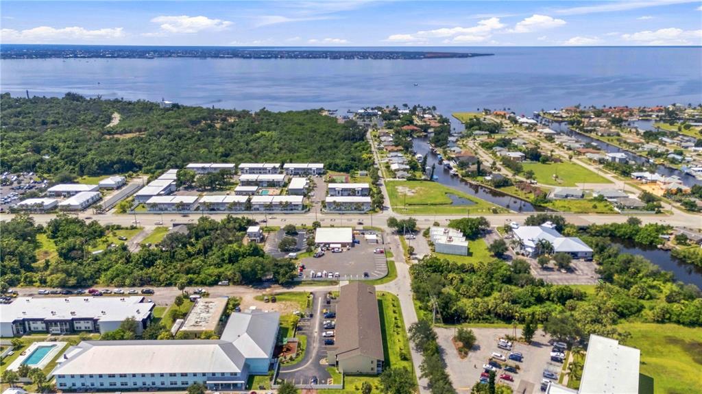 An aerial view shows apartment complexes, parking lots, and a canal leading to the water — 22278 VICK STREET UNIT A100, PORT CHARLOTTE, FL