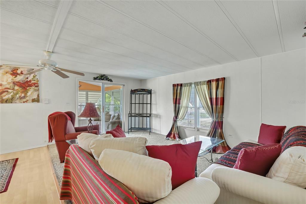 A living room features white walls, a ceiling fan, carpeted flooring, and a sliding glass door — 4809 EMPRESS LANE, HOLIDAY, FL