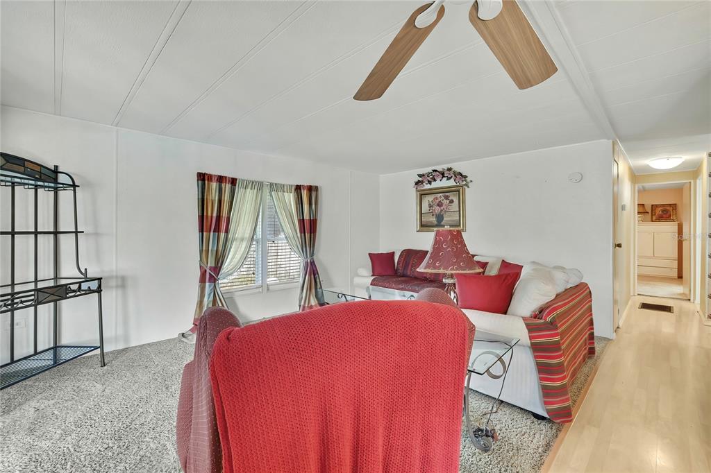 A living room features carpeted flooring, a ceiling fan, and a sofa with red pillows — 4809 EMPRESS LANE, HOLIDAY, FL