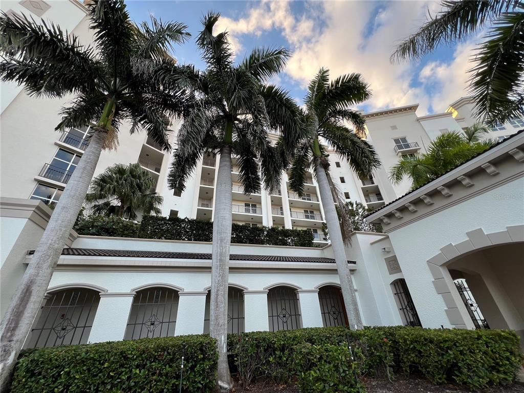 A low-angle view of a multi-story white building with palm trees and manicured hedges — 3321 SUNSET KEY CIRCLE UNIT 102, PUNTA GORDA, FL