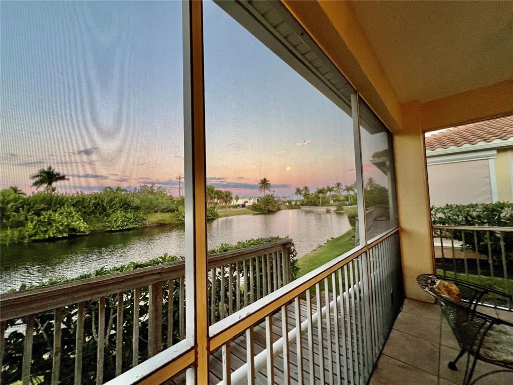 A screened-in balcony overlooks a canal at sunset with palm trees in the distance — 3321 SUNSET KEY CIRCLE UNIT 102, PUNTA GORDA, FL