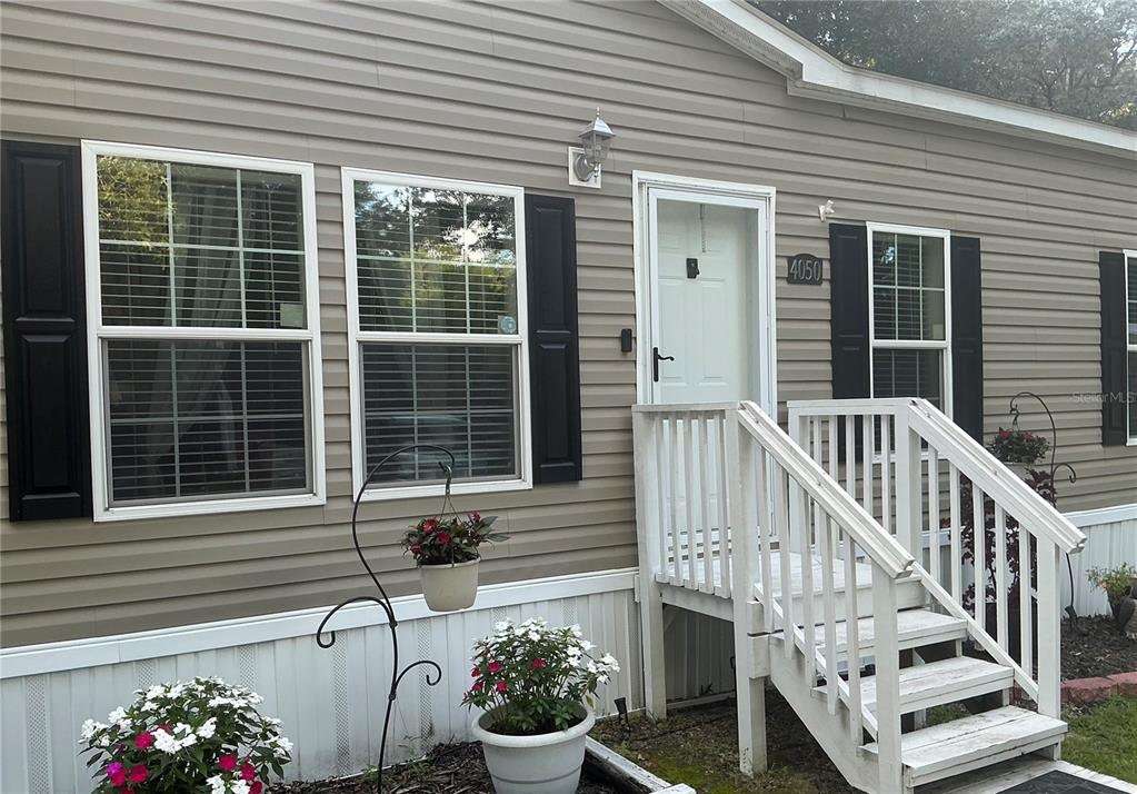 The exterior of a tan mobile home features white stairs, black shutters, and potted flowers — 4050 SW 178TH TERRACE, DUNNELLON, FL