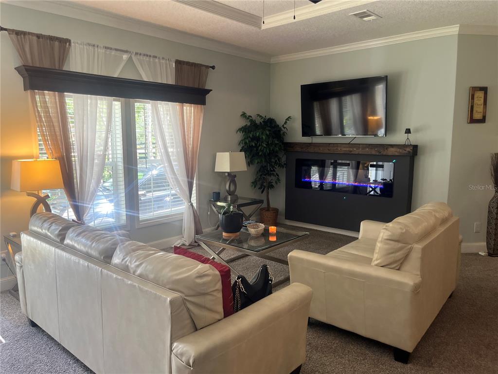 A living room features two cream-colored sofas, a glass coffee table, and a wall-mounted fireplace — 4050 SW 178TH TERRACE, DUNNELLON, FL
