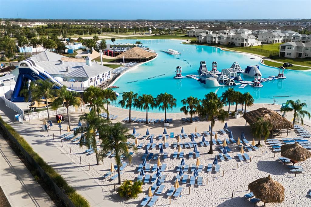 An aerial view shows a large turquoise lagoon with inflatable water obstacles and sandy beaches — 31575 BARREL WAVE WAY, WESLEY CHAPEL, FL
