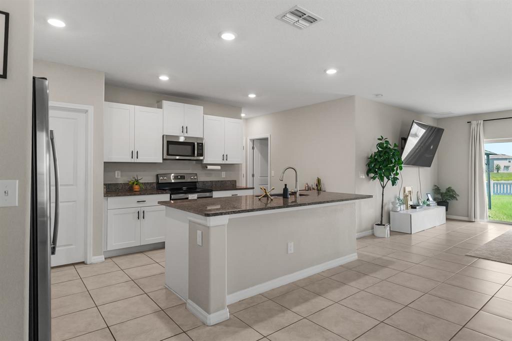 A kitchen with white cabinets, dark granite countertops, and an island opens to a living area — 31575 BARREL WAVE WAY, WESLEY CHAPEL, FL
