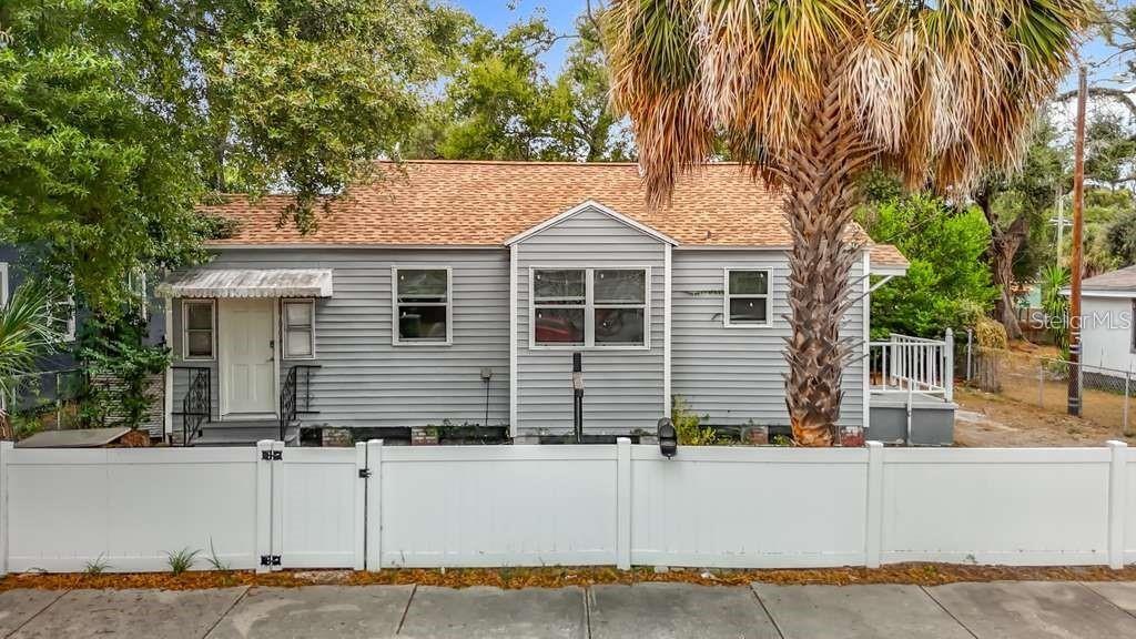 A gray, single-story house with a shingled roof stands behind a white vinyl fence — 1008 E 24TH AVENUE, TAMPA, FL