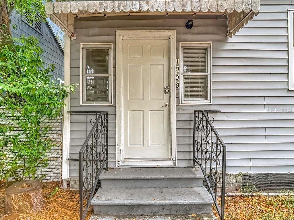 A gray house exterior features a white six-panel front door with metal railings and steps — 1008 E 24TH AVENUE, TAMPA, FL