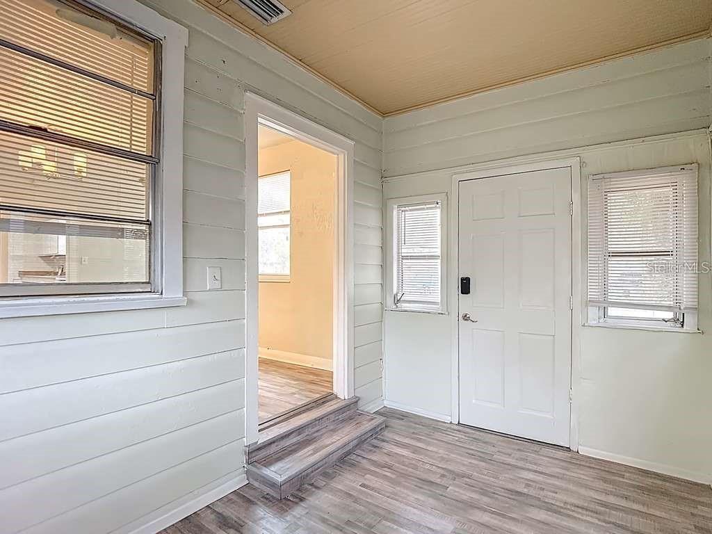 A sunroom with light-colored horizontal siding, wood-look flooring, and a doorway leading to another room — 1008 E 24TH AVENUE, TAMPA, FL