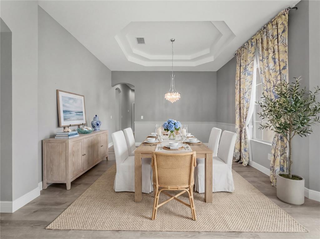 An empty dining room features gray walls, a tray ceiling, a chandelier, and wood flooring — 11530 OYSTER BAY CIRCLE, NEW PORT RICHEY, FL