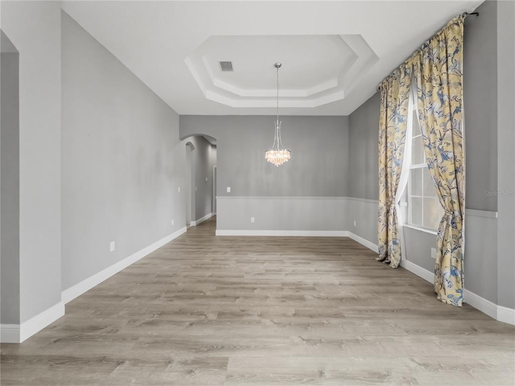An empty room with light wood-look flooring, gray walls, a crystal chandelier, and arched entryway — 11530 OYSTER BAY CIRCLE, NEW PORT RICHEY, FL
