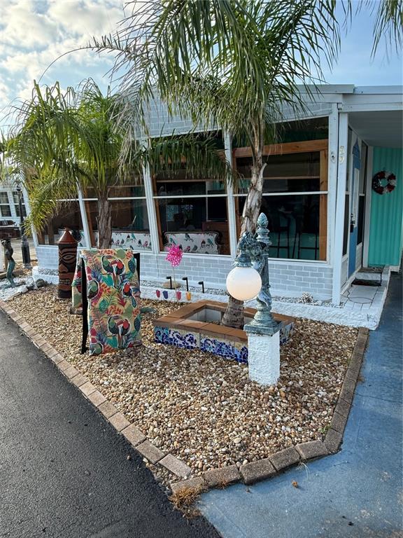An exterior view of a mobile home with a screened porch, palm trees, and gravel landscaping — 89 MERRIMAC DRIVE, FLAGLER BEACH, FL