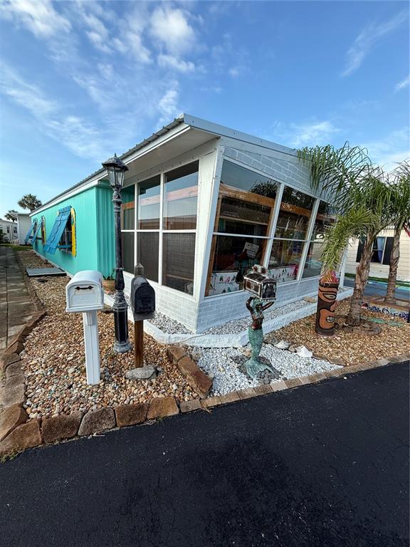 A turquoise mobile home features a white-framed sunroom, a decorative mermaid statue, and two mailboxes — 89 MERRIMAC DRIVE, FLAGLER BEACH, FL