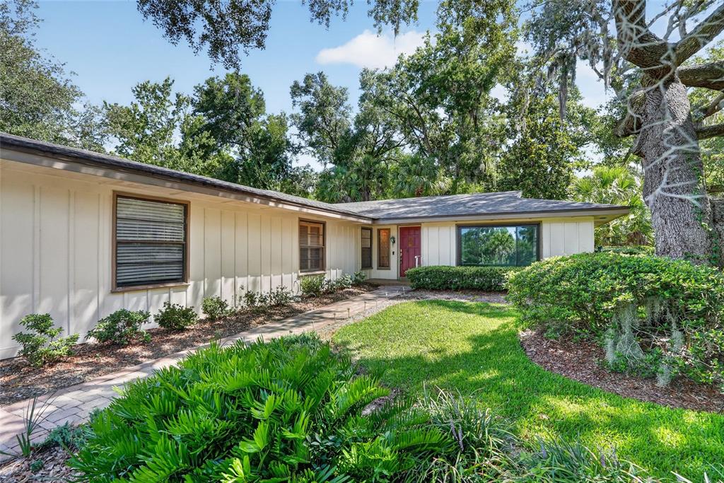 A single-story house with beige vertical siding, a red front door, and a landscaped yard — 2053 WOODY DRIVE, WINDERMERE, FL