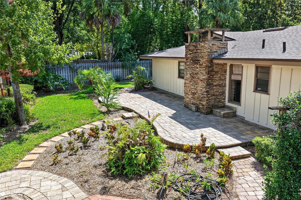 A stone chimney rises above a paved patio next to a house with light-colored siding — 2053 WOODY DRIVE, WINDERMERE, FL