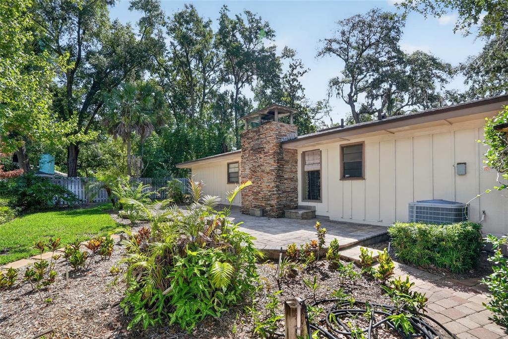 A backyard patio features a stone chimney, light-colored siding, and surrounding landscaping with trees — 2053 WOODY DRIVE, WINDERMERE, FL