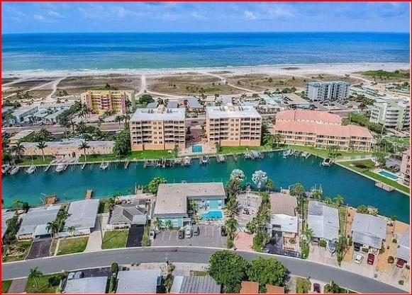 An aerial view shows a blue apartment building with a pool next to a canal — 11440 1ST STREET E UNIT 6, TREASURE ISLAND, FL