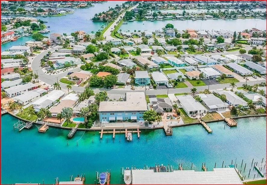 An aerial view shows a canal lined with residential buildings, boat docks, and swimming pools — 11440 1ST STREET E UNIT 6, TREASURE ISLAND, FL