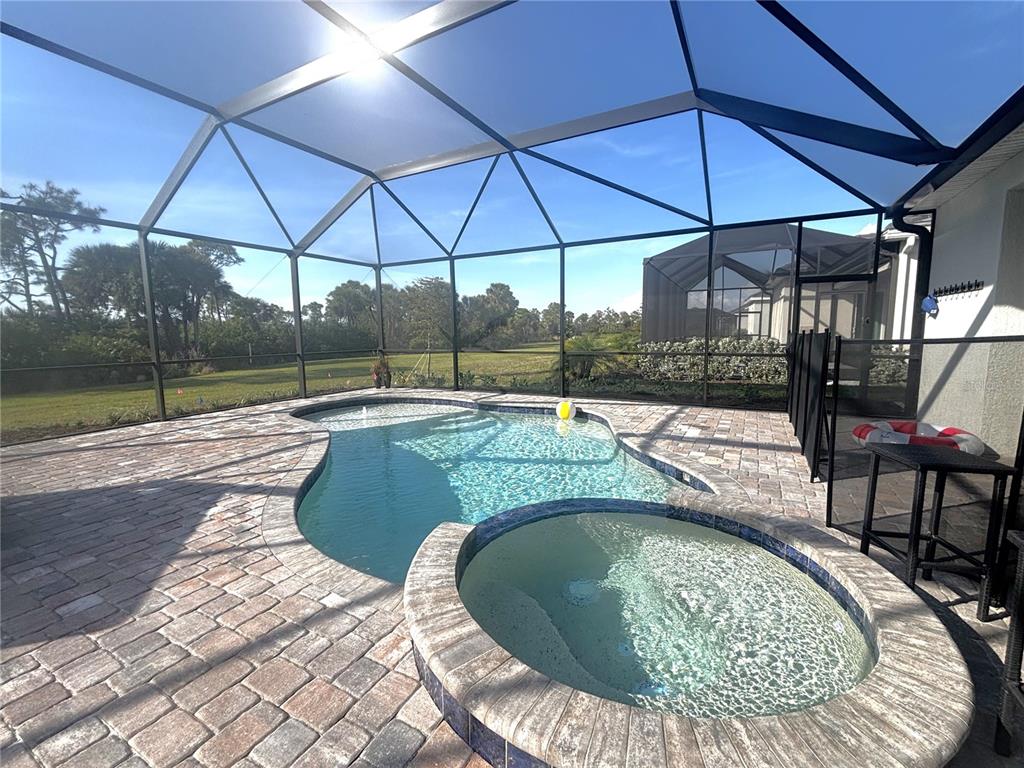 A screened-in patio features a swimming pool, a raised spa, and brick paver decking — 17455 JADESTONE COURT, VENICE, FL