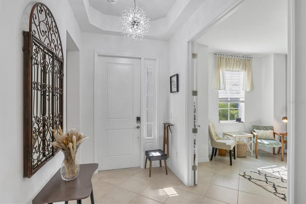 A bright entryway features tile flooring, a modern chandelier, and a doorway leading to a room — 17455 JADESTONE COURT, VENICE, FL
