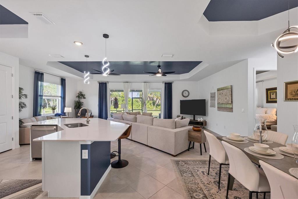 An open-concept living area features a kitchen island, dining table, and sectional sofa under tray ceilings — 17455 JADESTONE COURT, VENICE, FL