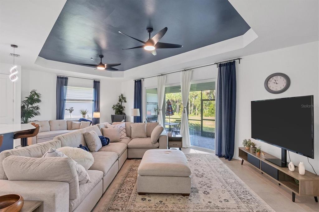 A living room features a large sectional sofa, a dark blue tray ceiling, and sliding glass doors — 17455 JADESTONE COURT, VENICE, FL