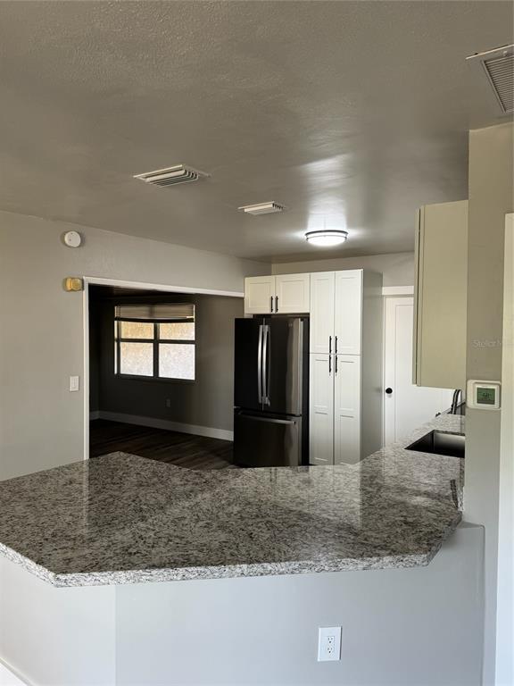 A kitchen with a granite peninsula, white cabinets, and a black refrigerator overlooks a room — 104 POCONO TRAIL W UNIT b, NOKOMIS, FL