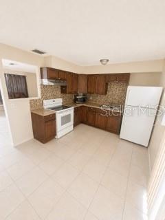 A kitchen with wood cabinets, tile flooring, white appliances, and a tiled backsplash — 729 LOTUS LANE, DAYTONA BEACH, FL
