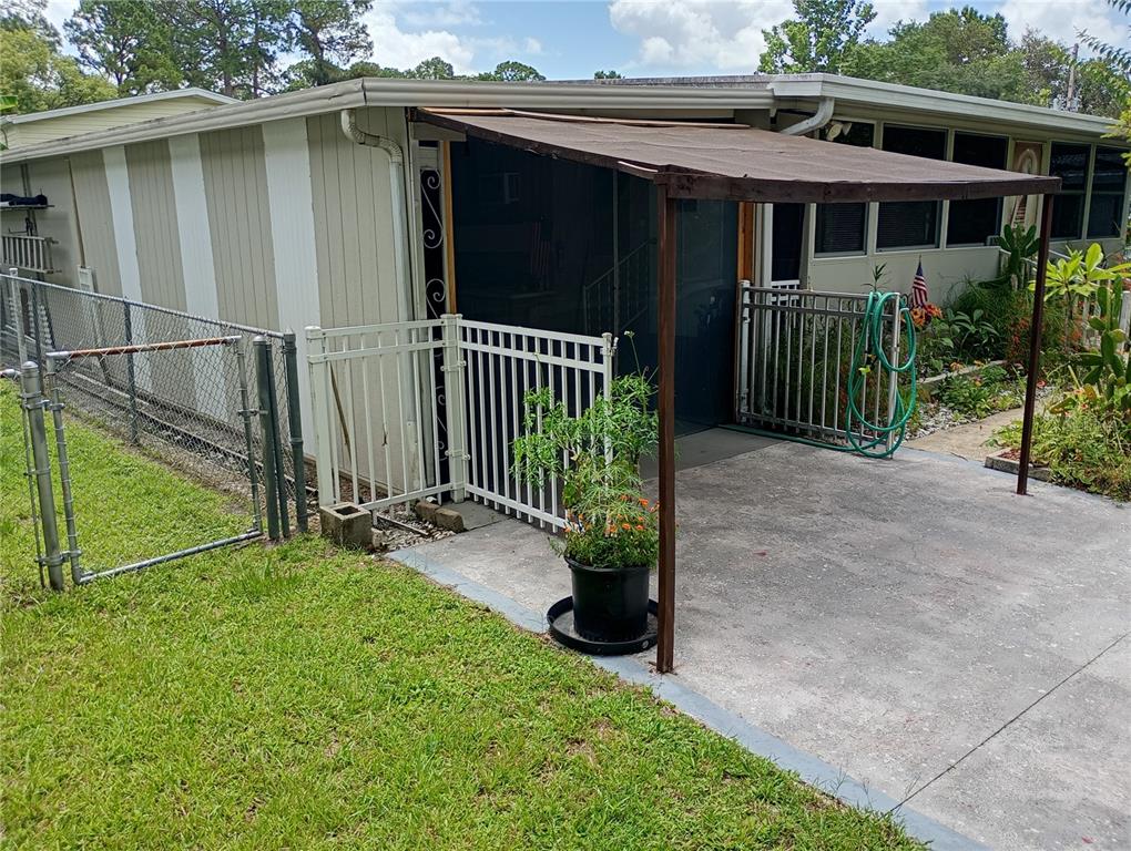 A mobile home exterior features a concrete patio, a metal awning, and white fencing — 109 FERN DRIVE, DEBARY, FL