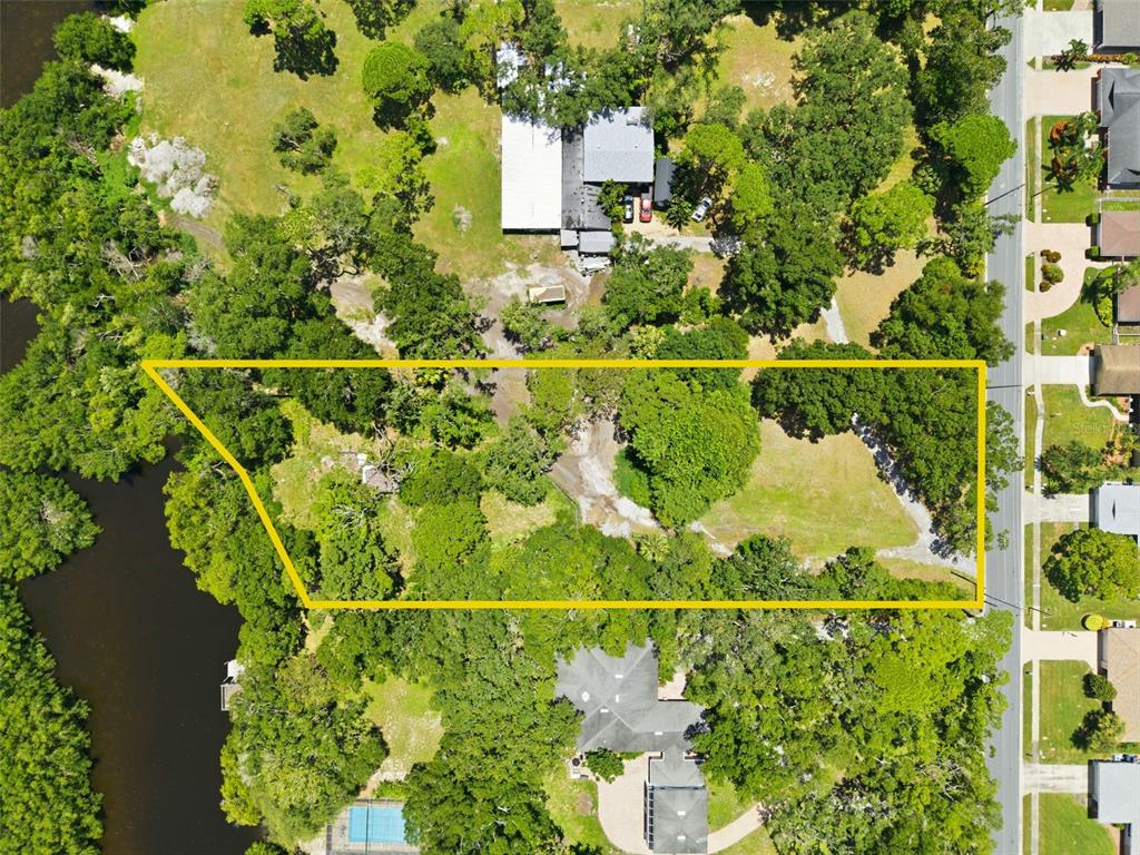 An aerial view shows a large, wooded residential lot outlined in yellow next to water — 6495 BURNING TREE DRIVE, SEMINOLE, FL