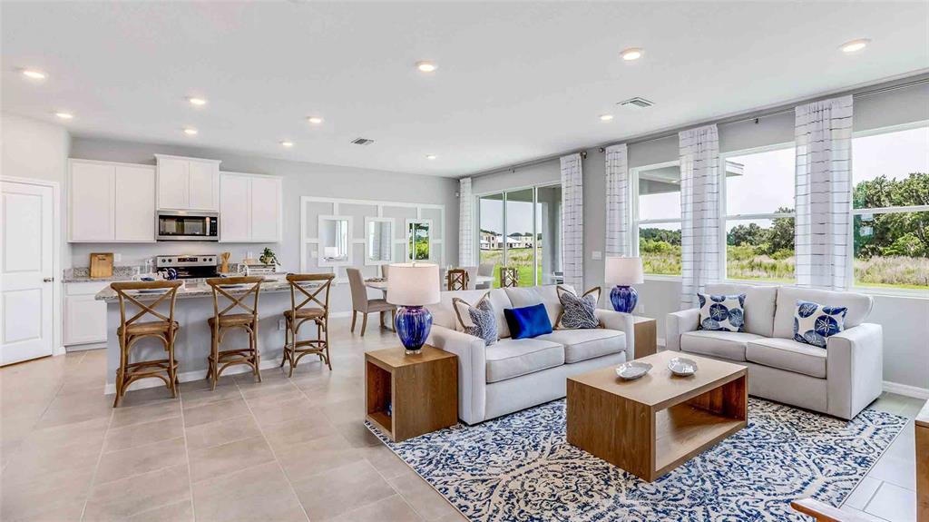 An open-concept kitchen and living area features white cabinetry, tile flooring, and neutral furniture — 35600 LOWERY TRAIL, ZEPHYRHILLS, FL