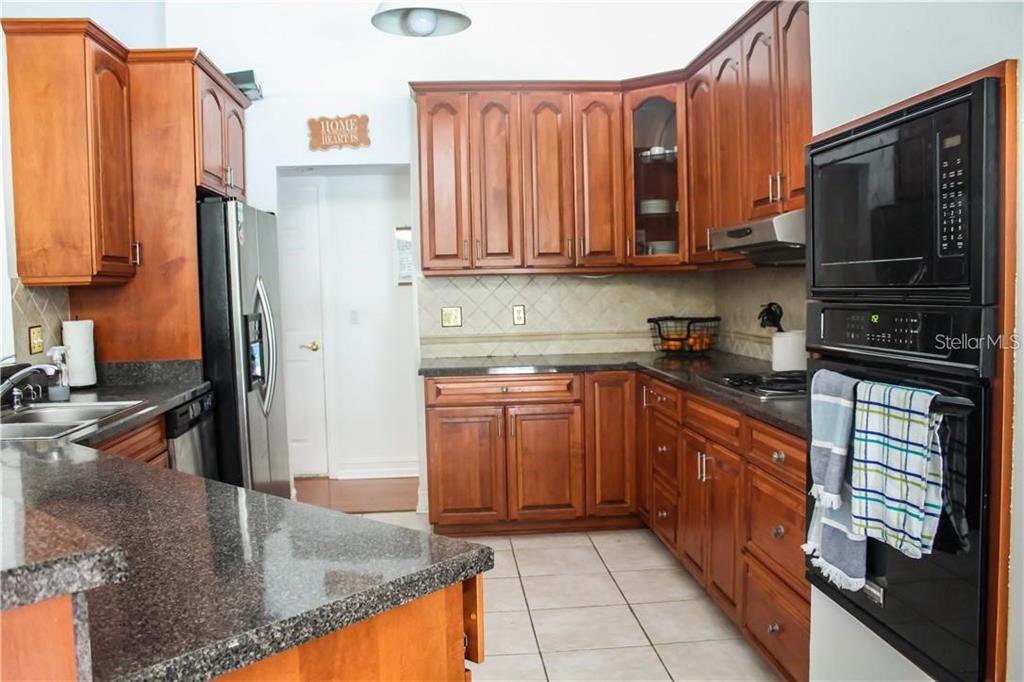 A kitchen with wood cabinets, dark granite countertops, stainless steel appliances, and tile flooring — 2630 STANTON HALL COURT, WINDERMERE, FL