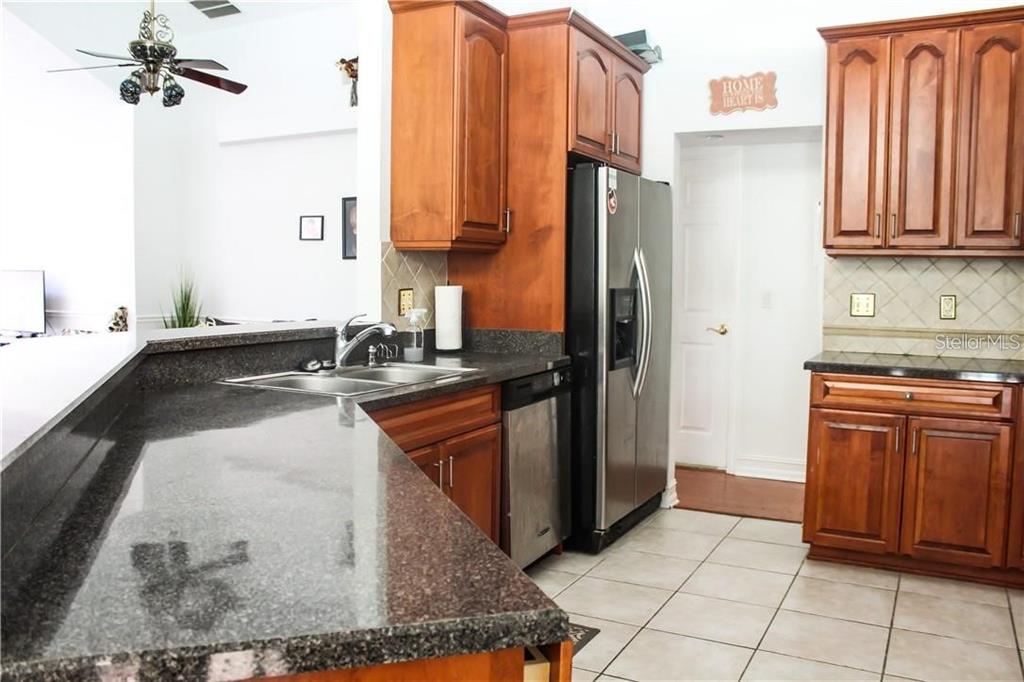 A kitchen features dark granite countertops, cherry wood cabinets, stainless steel appliances, and tile flooring — 2630 STANTON HALL COURT, WINDERMERE, FL