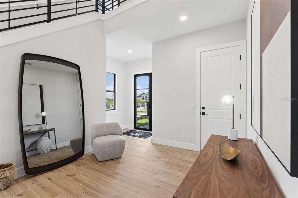 A modern entryway features light wood flooring, a large floor mirror, and a white door — 16308 VETTA DRIVE, MONTVERDE, FL