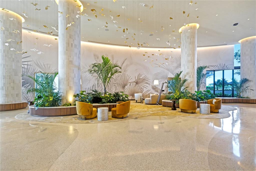 A spacious hotel lobby features large stone columns, indoor plants, and gold-colored accent chairs — 5100 COCONUT ROAD UNIT 705, ESTERO, FL