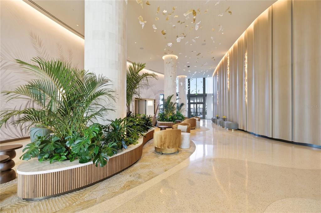 A modern hotel lobby features tall columns, indoor planters, and a decorative ceiling light installation — 5100 COCONUT ROAD UNIT 705, ESTERO, FL