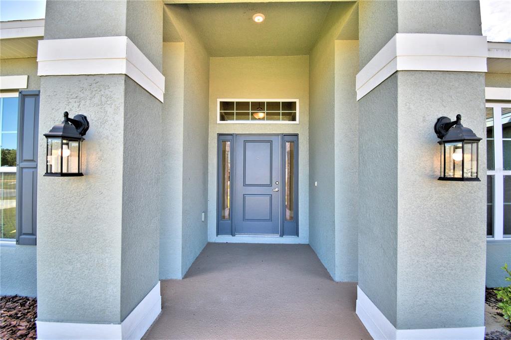 A covered entryway features a gray front door with sidelights and two black wall lanterns — 4615 CALAMINT LANE, AUBURNDALE, FL
