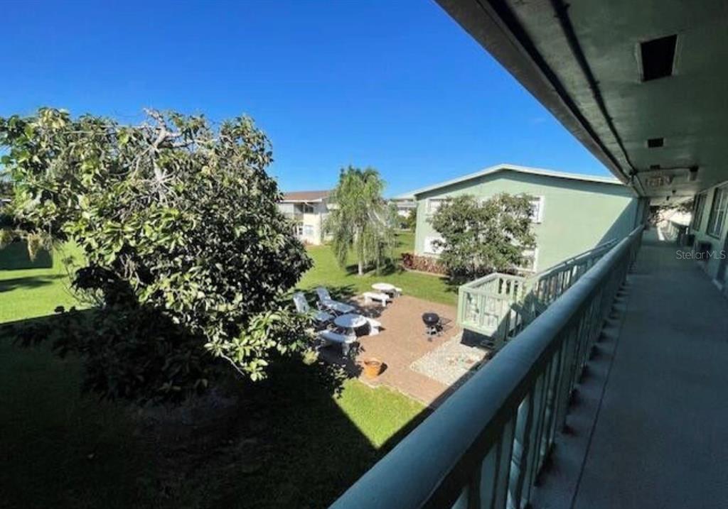 An elevated view from a balcony overlooking a grassy courtyard with patio furniture and trees — 66 EASTHAMPTON UNIT C, WEST PALM BEACH, FL
