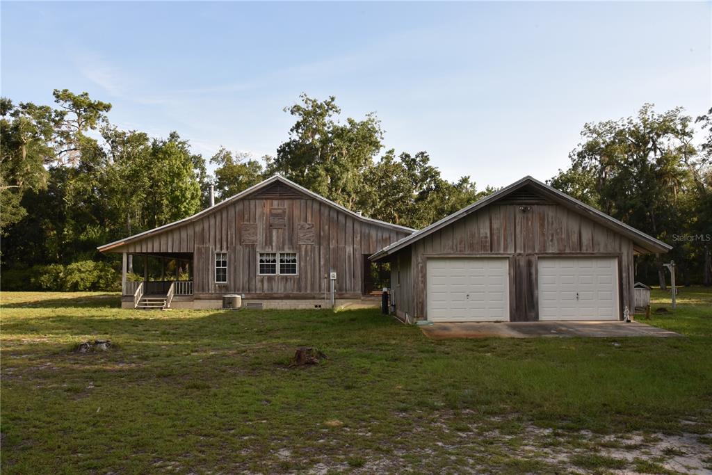 A rustic wooden house with a two-car garage and a covered porch sits on grass — 5351 SW COUNTY ROAD 347, CEDAR KEY, FL