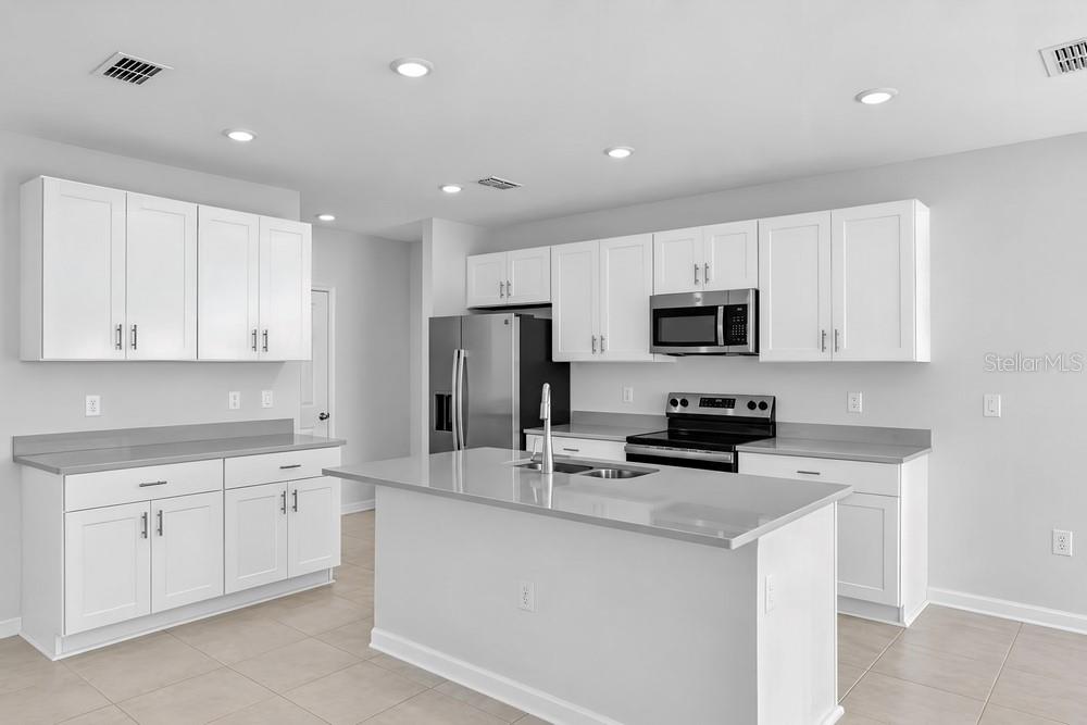 A modern kitchen features white cabinetry, stainless steel appliances, and a large central island — 13840 SHELLMORE AVENUE, PALMETTO, FL